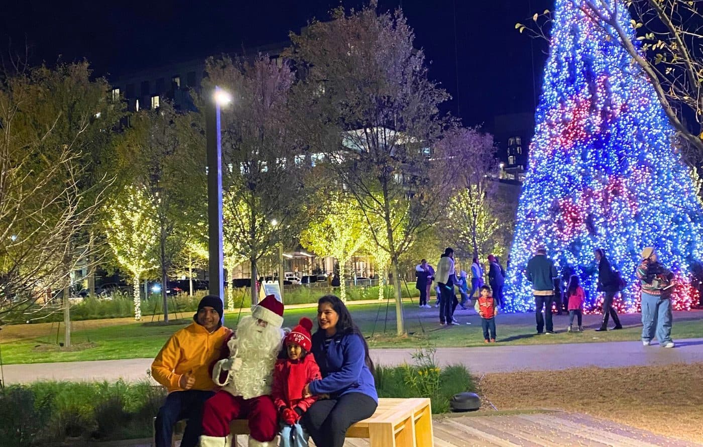 Family posing with Santa beside the lit holiday tree at night